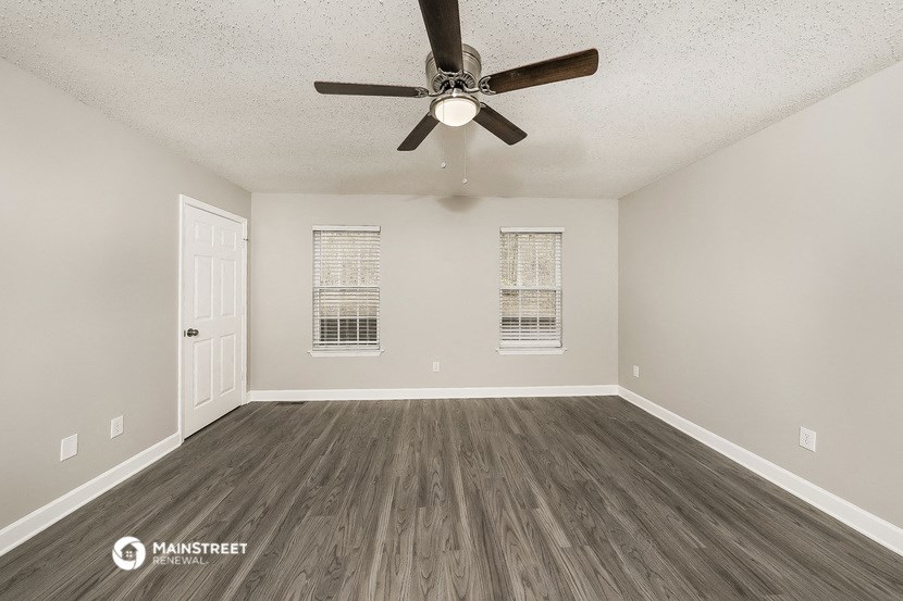 the spacious living room of an empty home with a ceiling fan