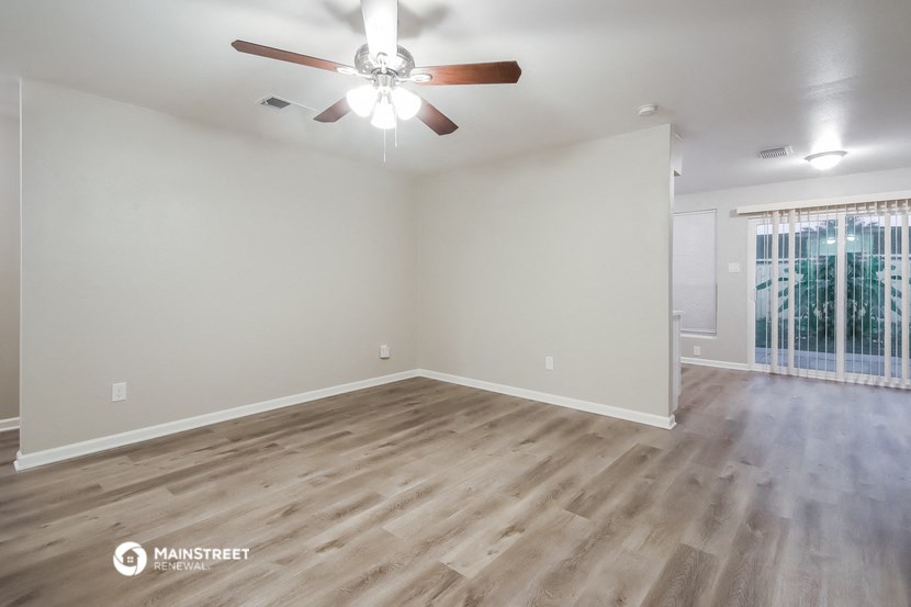 the spacious living room with wood flooring and a ceiling fan