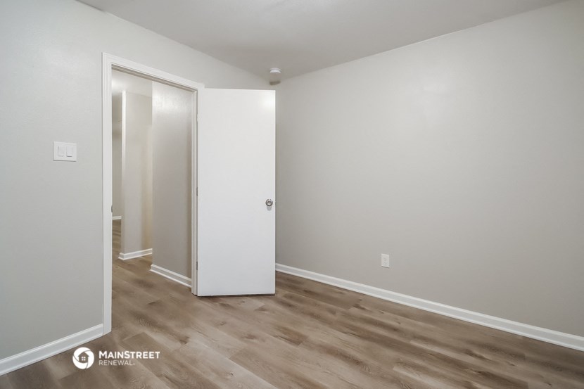 a bedroom with white walls and wood flooring and a closet