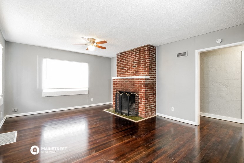 an empty living room with a brick fireplace and wooden floors