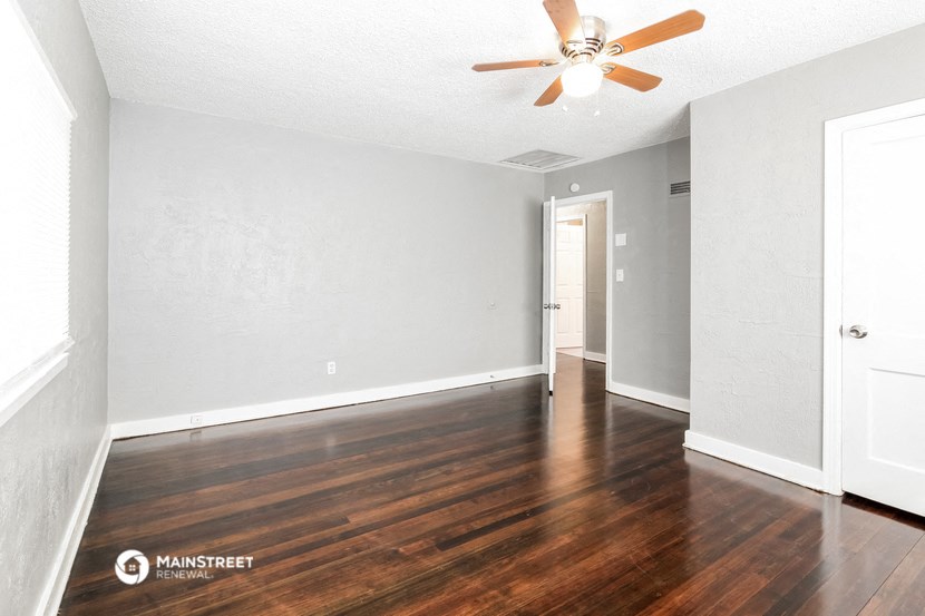 the spacious living room with hardwood flooring and a ceiling fan
