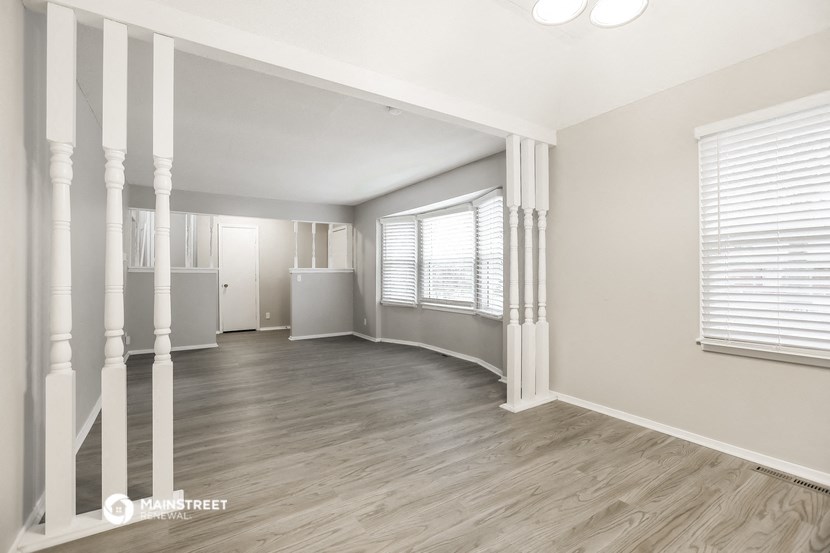the living room and dining room of an apartment with wood floors and white pillars