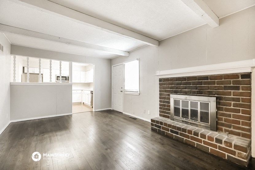 an empty living room with a brick fireplace and a kitchen