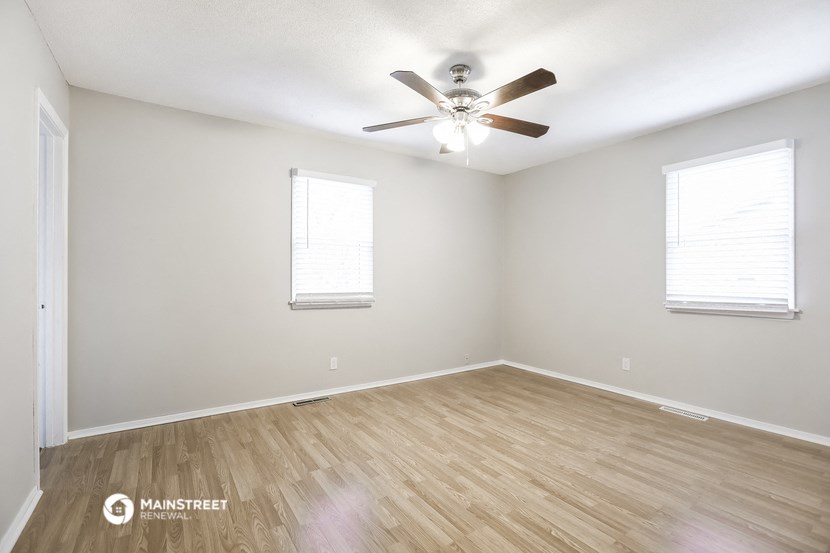 the spacious living room with wood flooring and a ceiling fan