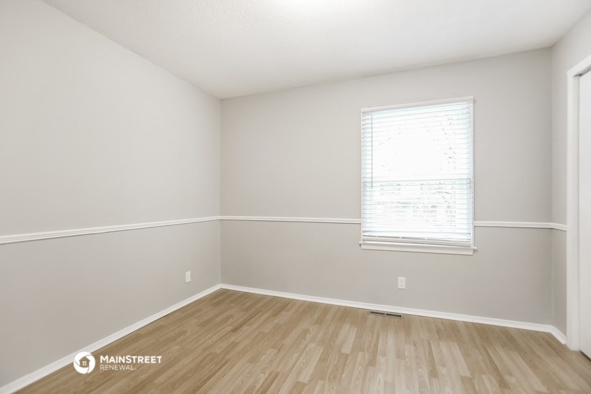 a bedroom with white walls and wood floors and a window
