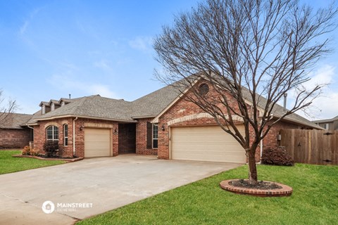 a brick house with two garage doors and a tree in the driveway
