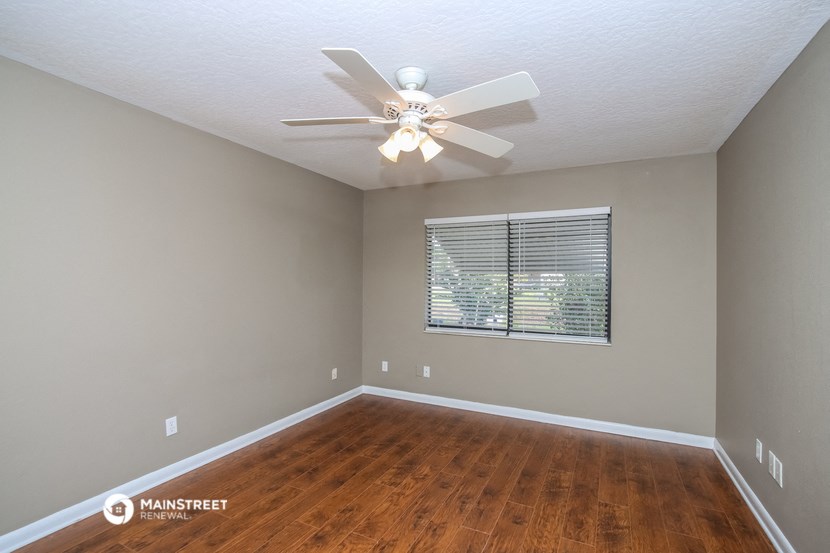 the spacious living room with hardwood flooring and a ceiling fan
