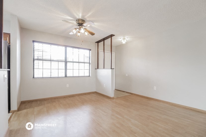 the spacious living room with a large window and a ceiling fan