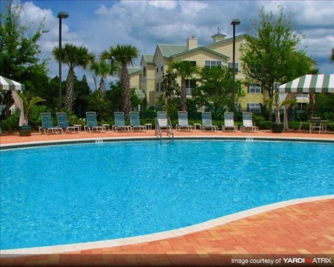 a large swimming pool with chairs and a building in the background
