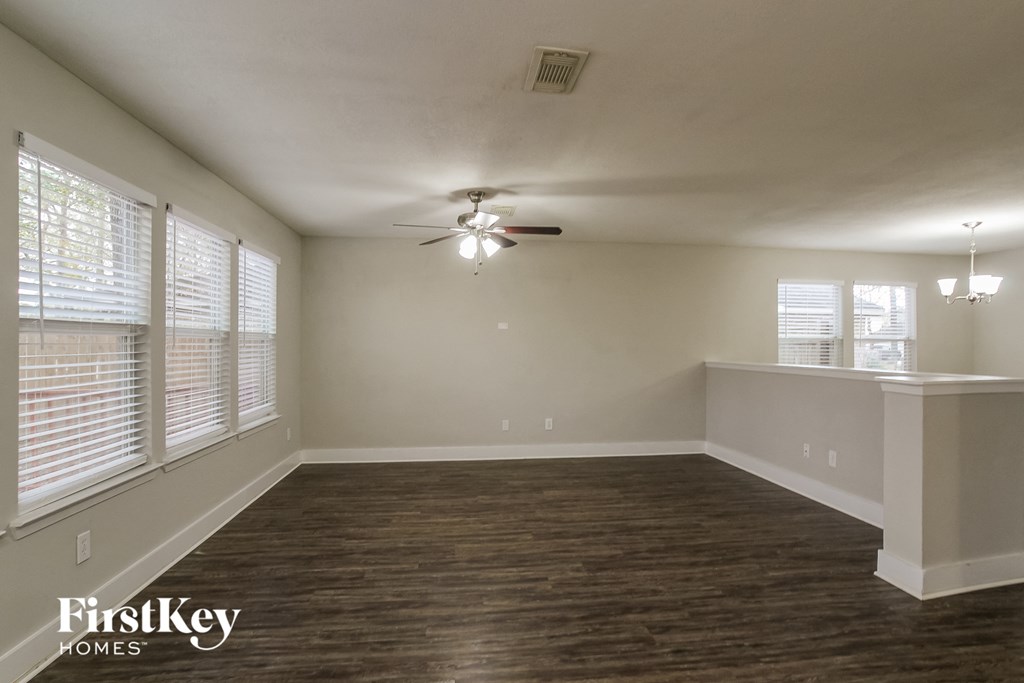an empty living room with a ceiling fan and large windows