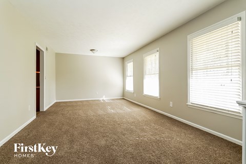 an empty living room with a carpeted floor and three windows