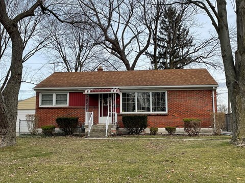 a small red brick house with a yard and trees