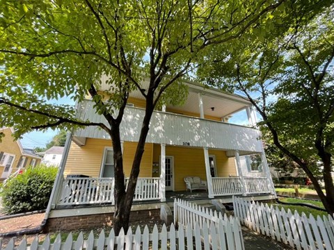 A yellow house with a white picket fence and a tree in front.