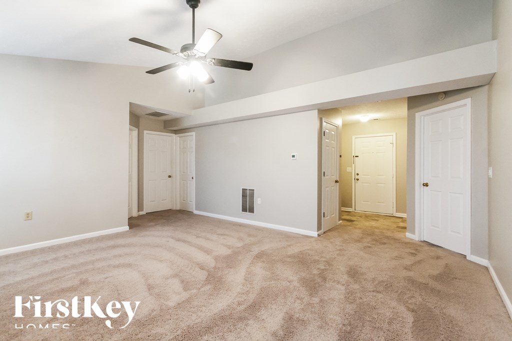 A carpeted room with a ceiling fan and two doors.