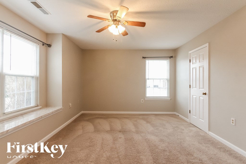 A room with a carpet floor, a ceiling fan, and a door.