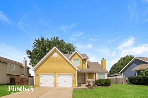 a yellow house with white garage doors and a green lawn