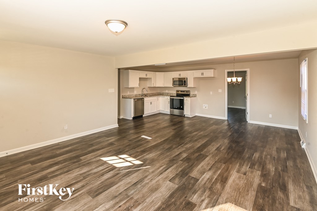 A spacious living room with wooden flooring and a kitchen in the background.