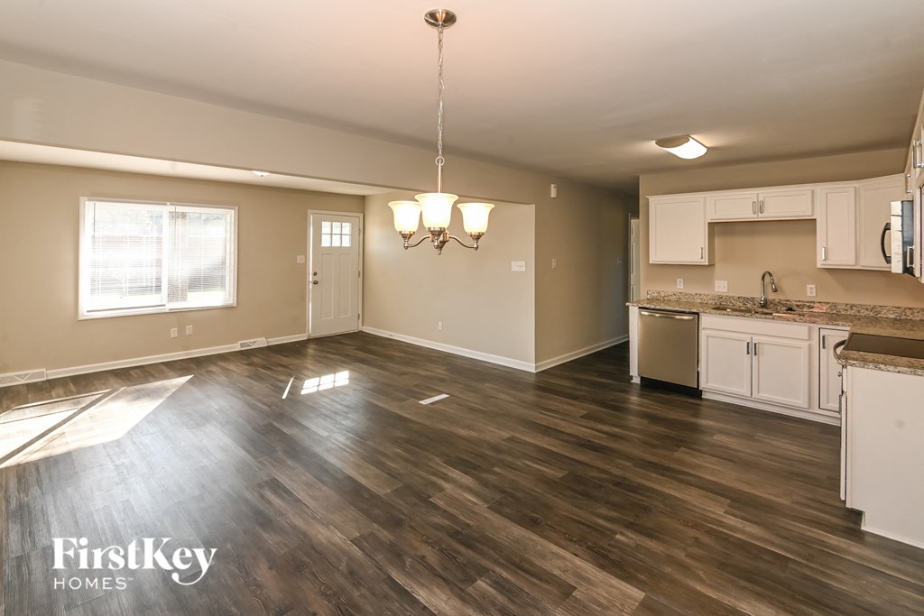 A well-lit, empty room with a kitchen area visible in the background.