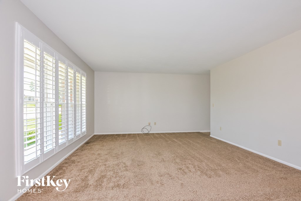 a spacious living room with white walls and a large window with shutters