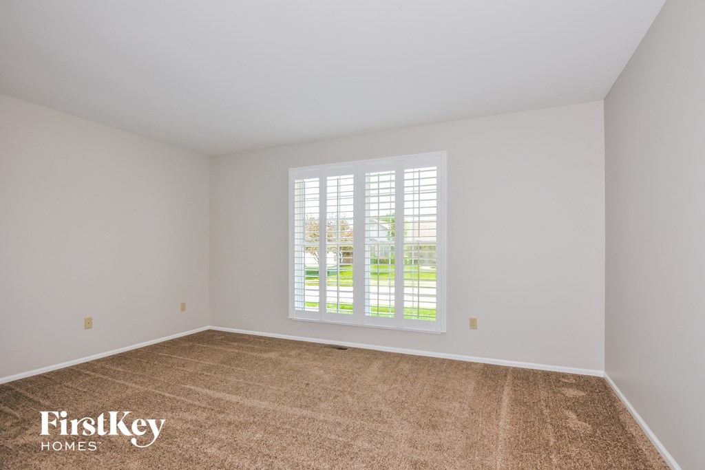 the living room of an empty home with a large window and carpet