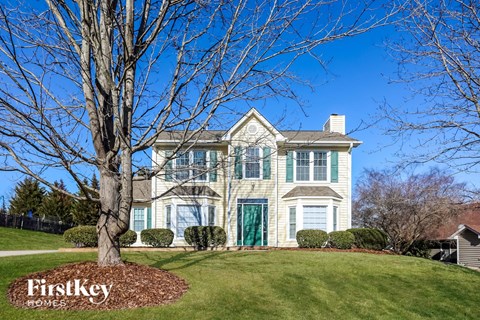 a white house with green shutters and a large tree on a hill