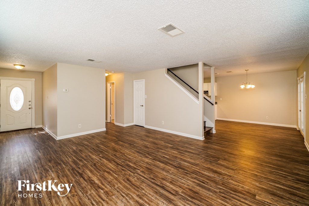 A spacious room with wooden flooring and a staircase in the background.