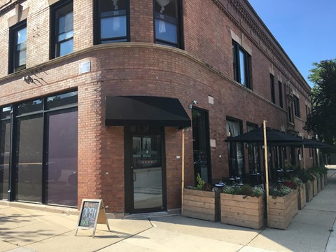 A red brick building with a black awning and a sign on the sidewalk.