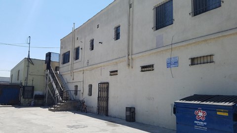 the side of a white building with a staircase and a blue container