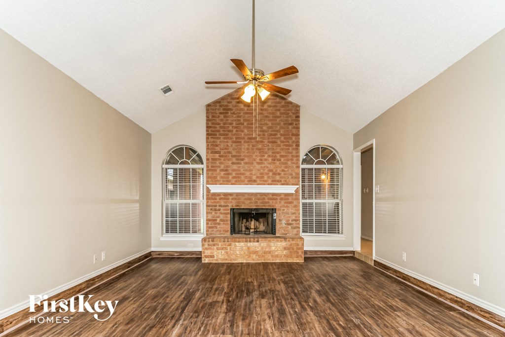 an empty living room with a brick fireplace and a ceiling fan
