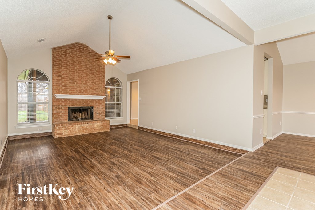an empty living room with a brick fireplace and wooden floors
