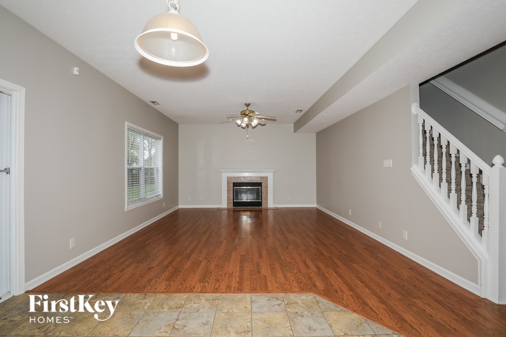 A spacious room with wooden floors and a staircase on the right side.