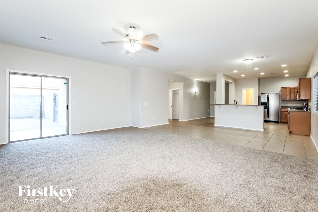 an empty living room with a kitchen and a ceiling fan