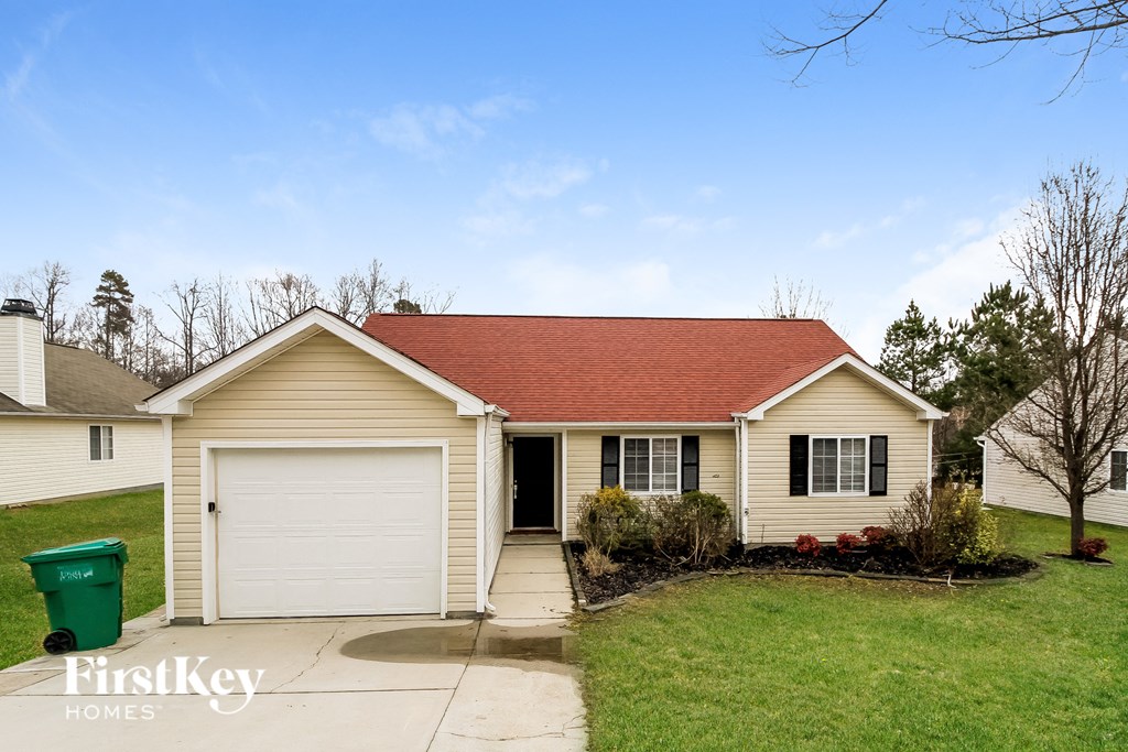 A house with a red roof and a green trash bin in front of it.
