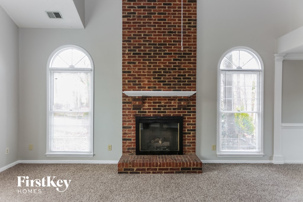 A room with a brick fireplace and two windows.