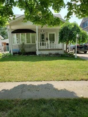 A white house with a porch and a tree in front.