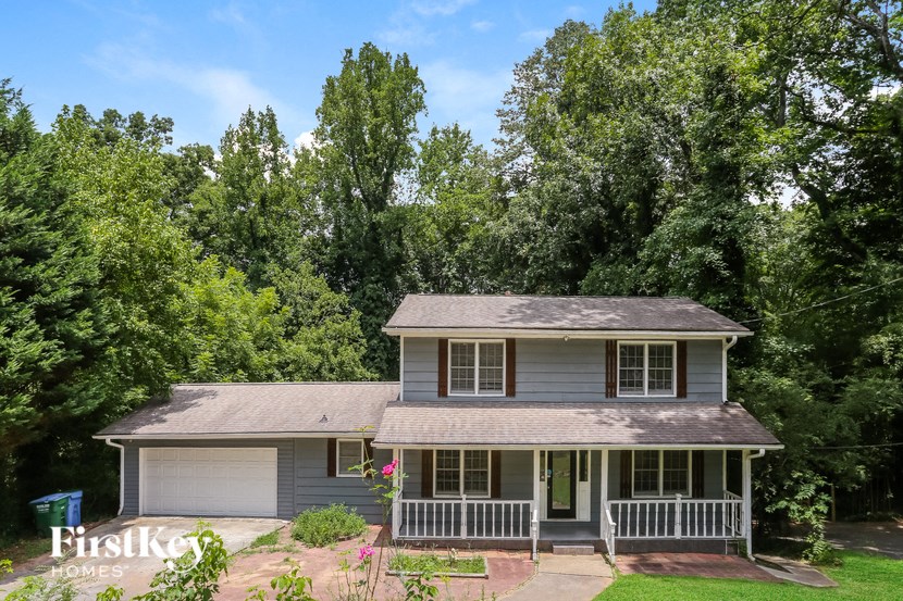a small gray house with a porch and trees