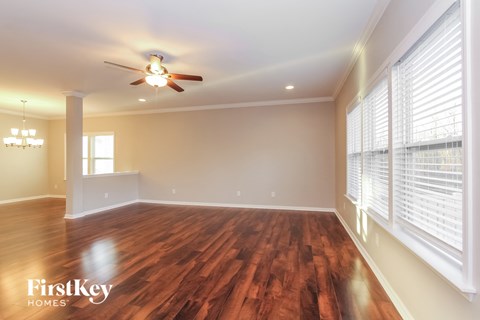 an empty living room with a ceiling fan and large windows