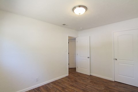 a bedroom with white walls and wood flooring and a closet