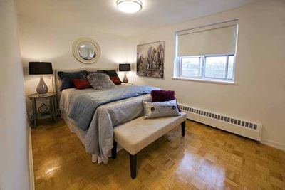Bayview Apartments Elegant bedroom with plush duvet draped against the foot of the bed. Two night tables are on either side of the bed in Richmond Hill, ON