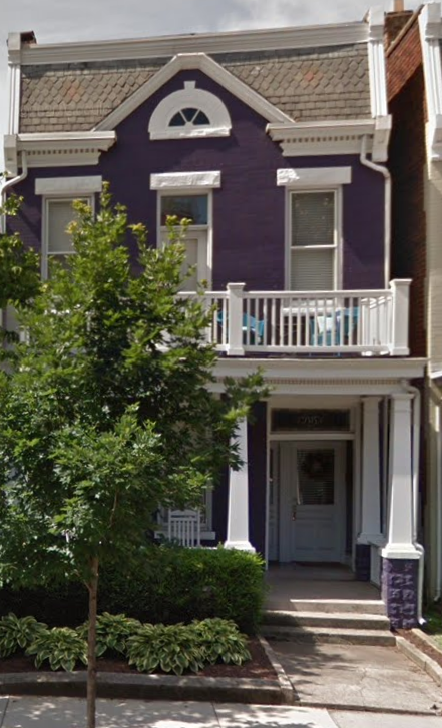 a purple house with a balcony and a tree in front
