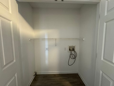 A white closet with a wooden floor and a hanger rack.