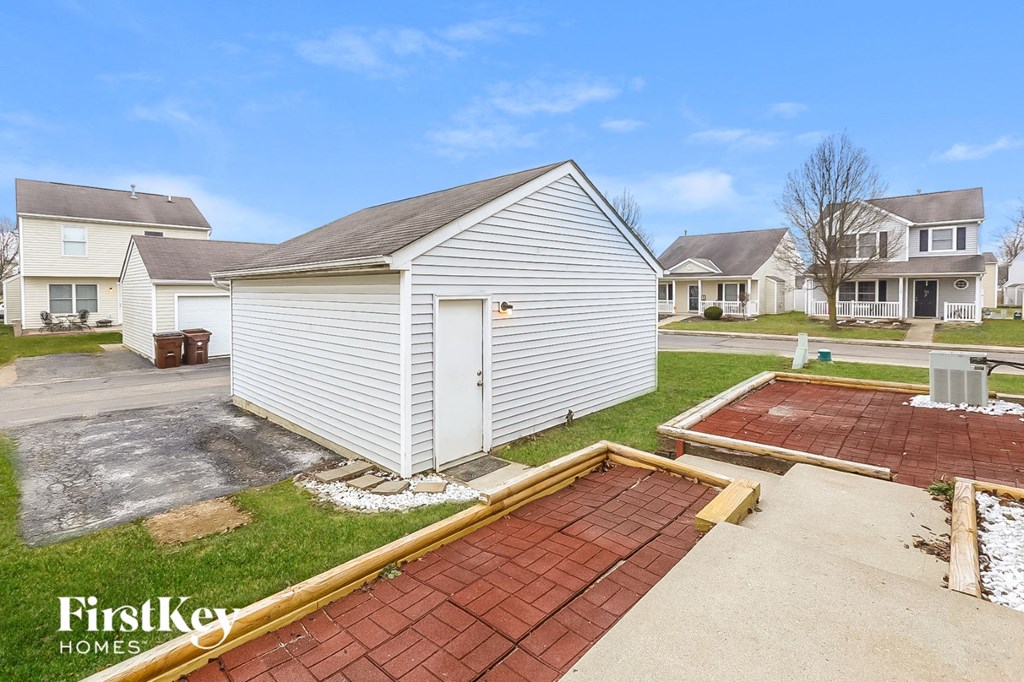 a small white shed on the side of a driveway in front of some houses