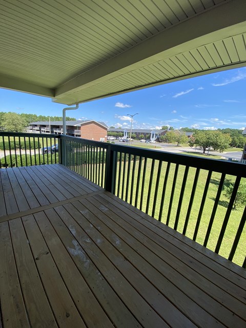 A wooden deck with a metal railing overlooks a grassy area.