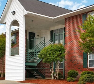 A white house with a red brick exterior and a green staircase.