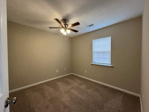 an empty bedroom with a ceiling fan and a window