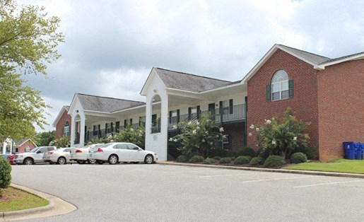 A red brick building with a white entrance and cars parked in front.