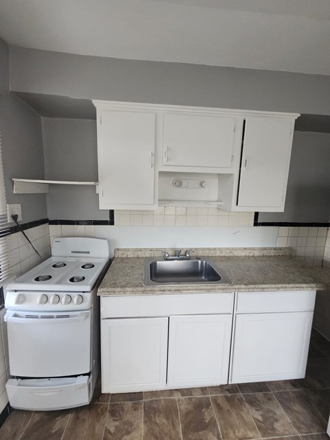 A white kitchen with a stove, sink, and cabinets.
