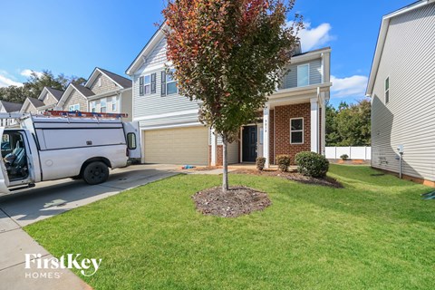 A tree with red leaves is in the front yard of a house with a white van parked in front.
