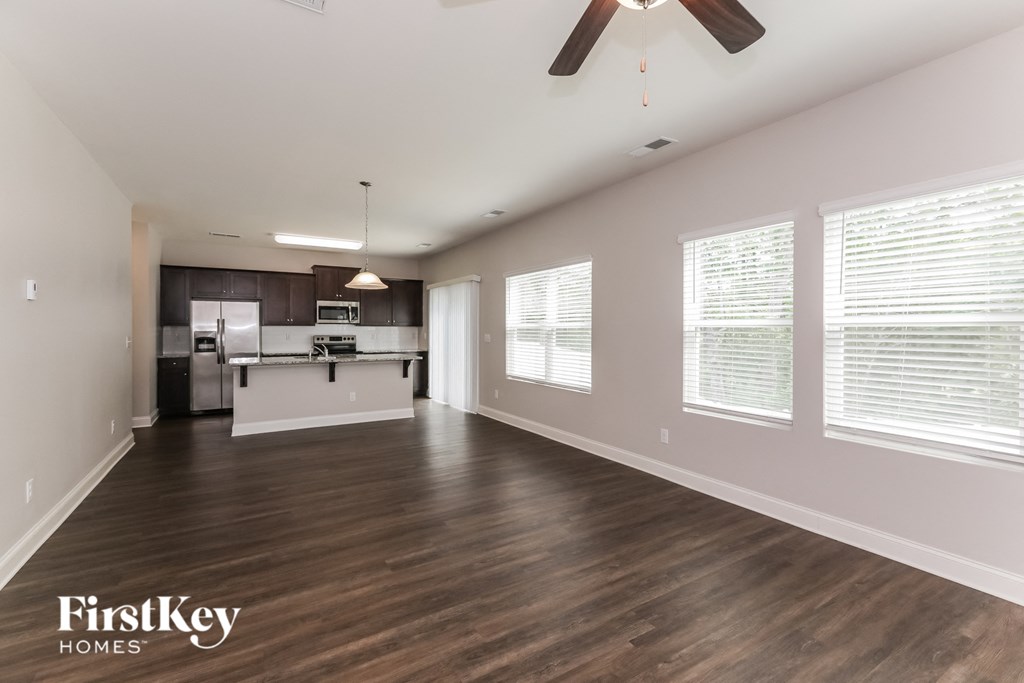 an empty living room with a kitchen and a ceiling fan