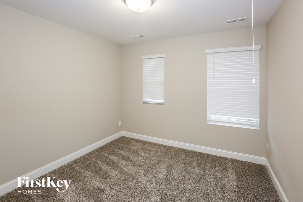 A room with a carpeted floor and two windows with blinds.